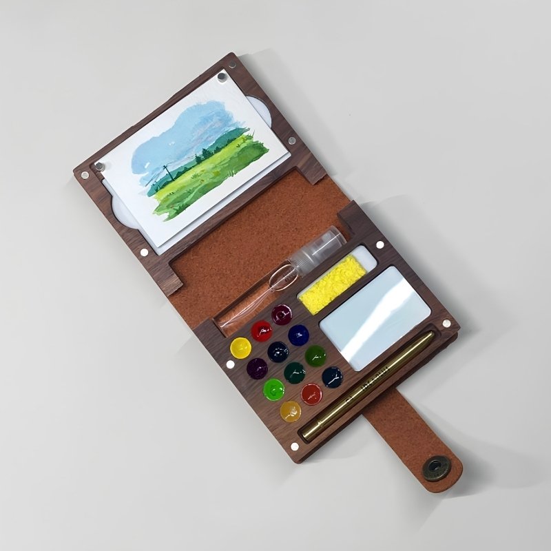 Open ArtMate walnut folio art kit with a landscape painting, 12 round paint pans, telescopic brush and water vial